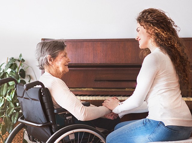 A girl with grandmother in wheelchair by the piano.