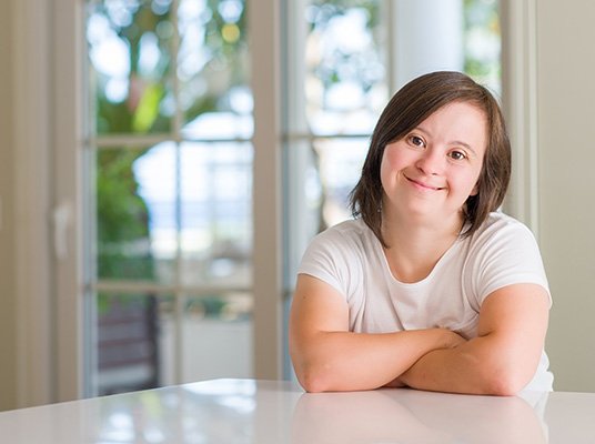 Down syndrome woman at home happy face smiling with crossed arms looking at the camera. Positive person.